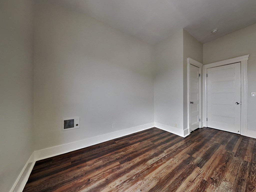 a bedroom with white walls and wood flooring and a door