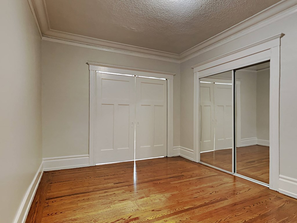 a bedroom with mirrored closet doors and a wood floor