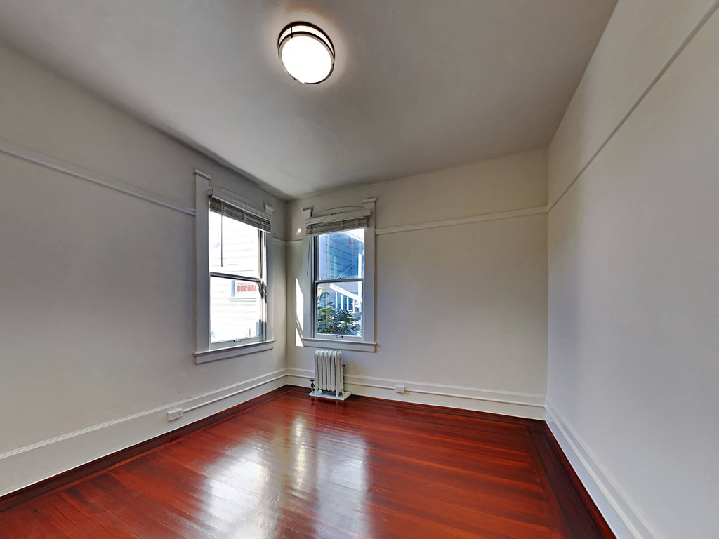 an empty room with wood floors and two windows