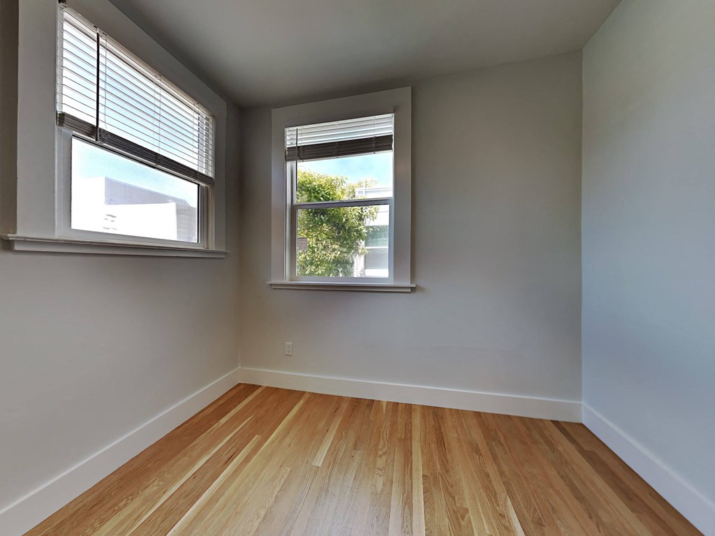 an empty room with two windows and wood floors