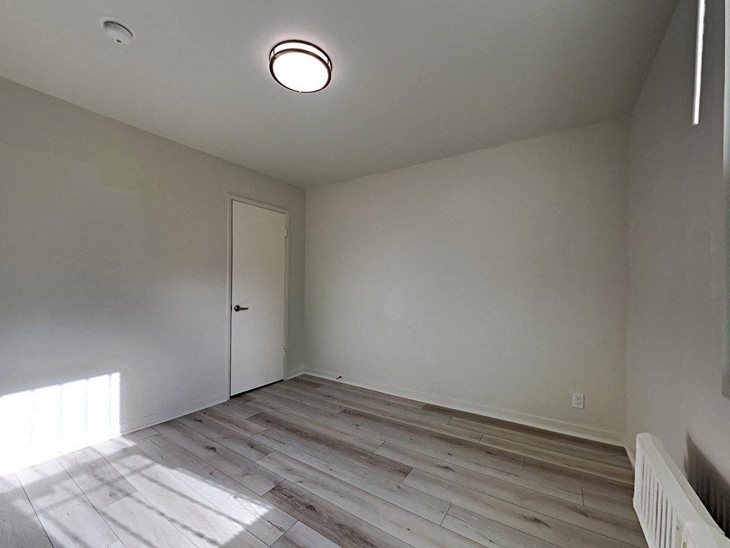 a bedroom with white walls and wood flooring and a door