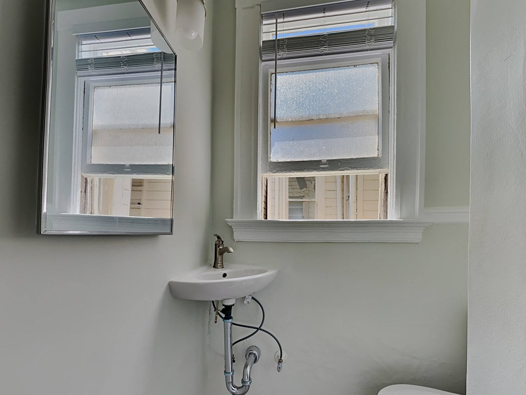 a small bathroom with a sink and two windows