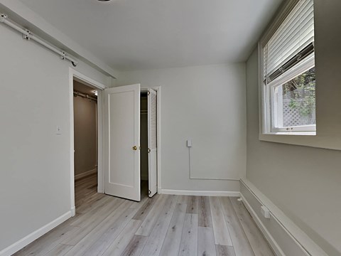 a bedroom with white walls and wood floors and a door to a closet