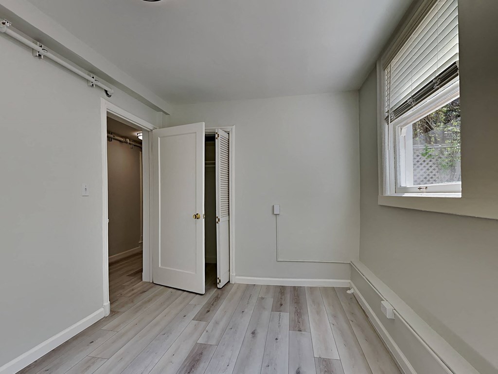 a bedroom with white walls and wood floors and a door to a closet