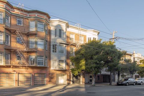 A row of apartment buildings with cars parked in front.