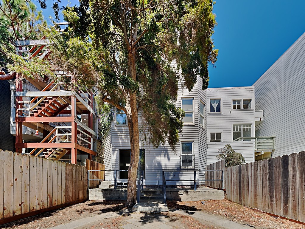 the exterior of an apartment building with a tree and a wooden fence