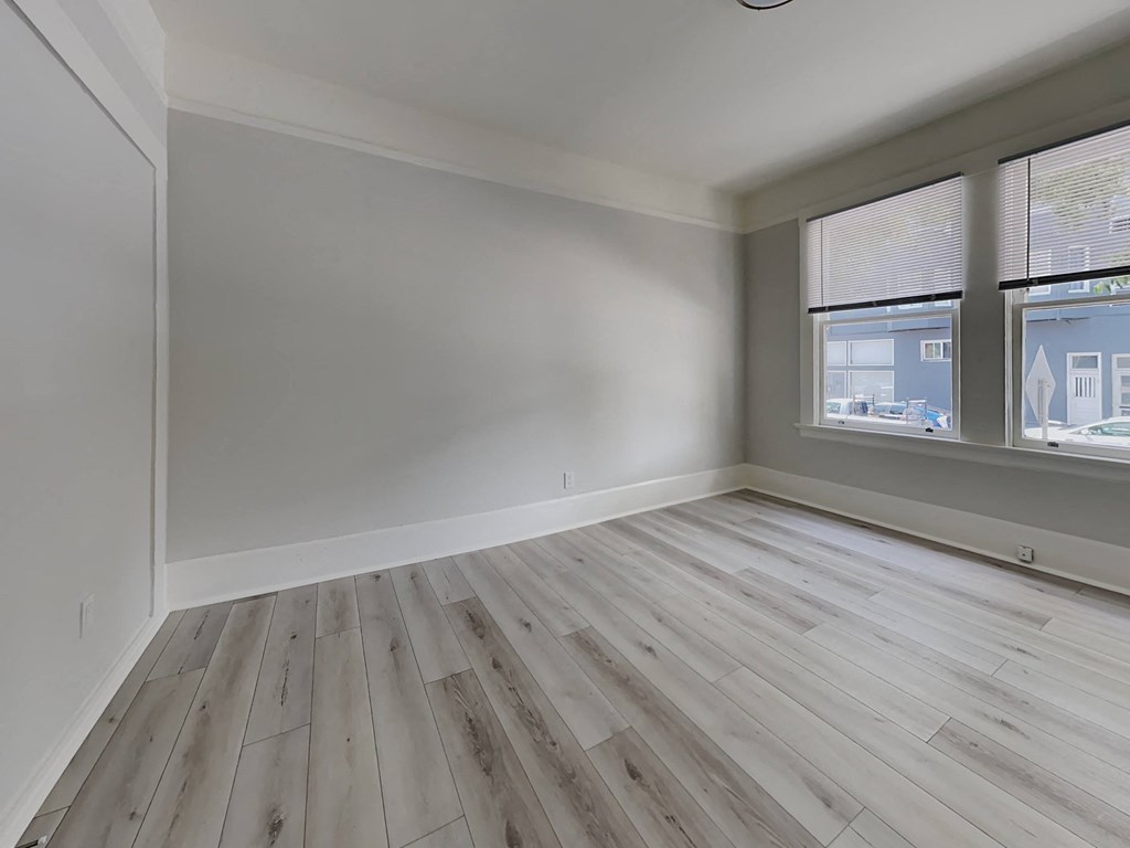 an empty room with wood flooring and two windows