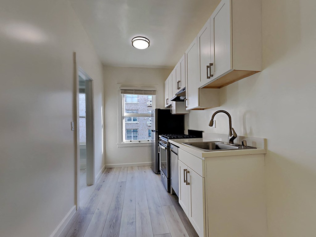 an empty kitchen with white cabinets and a window