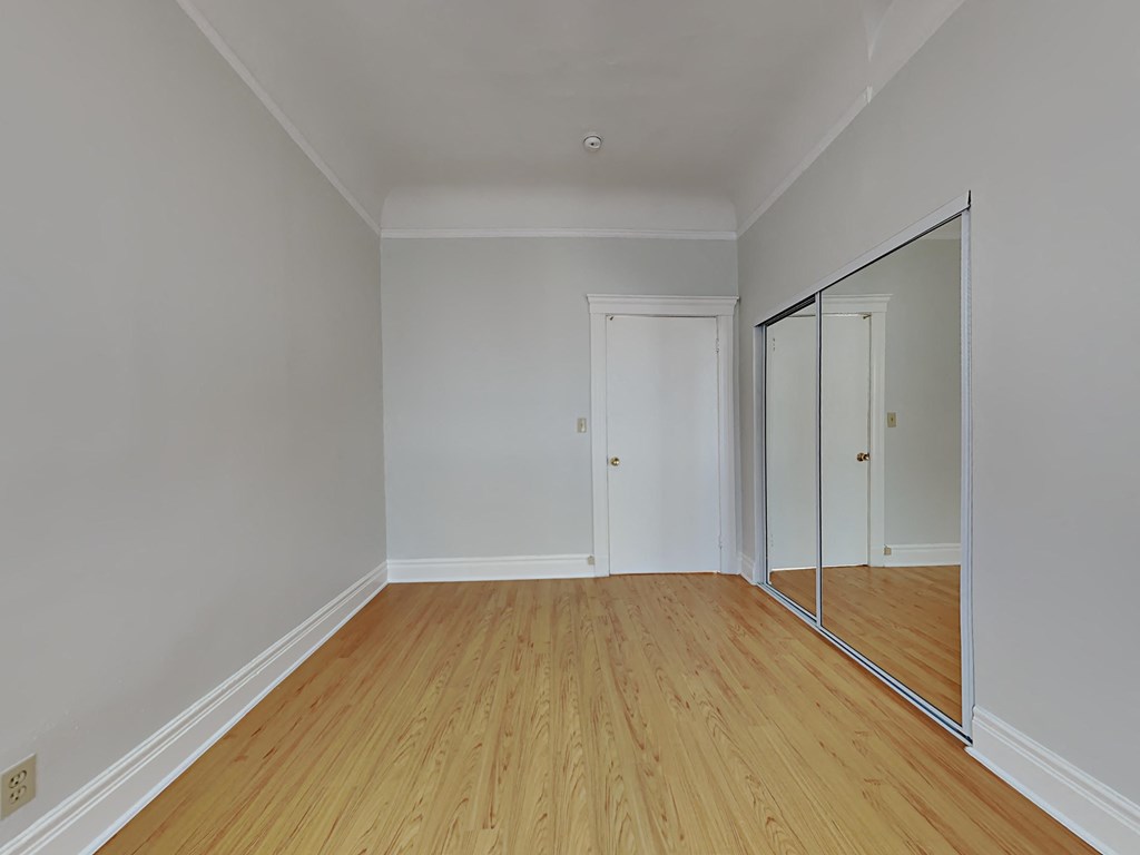 a bedroom with mirrored closet doors and a hard wood floor