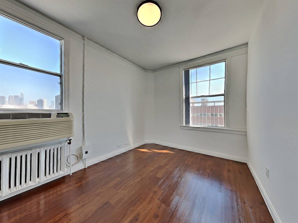 an empty living room with wood floors and a radiator and two windows