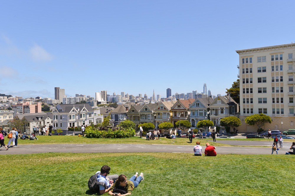 people sitting on the grass in a park in front of houses