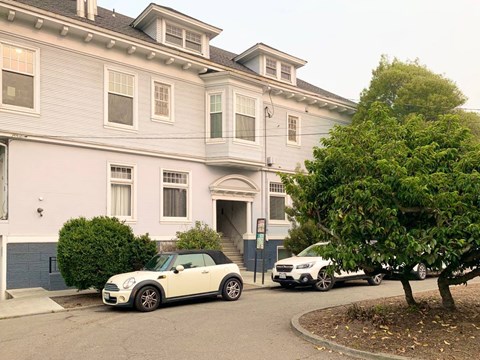 A white car is parked in front of a grey building.