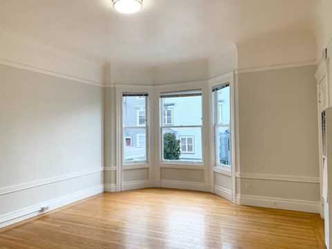 an empty living room with three windows and wood floors