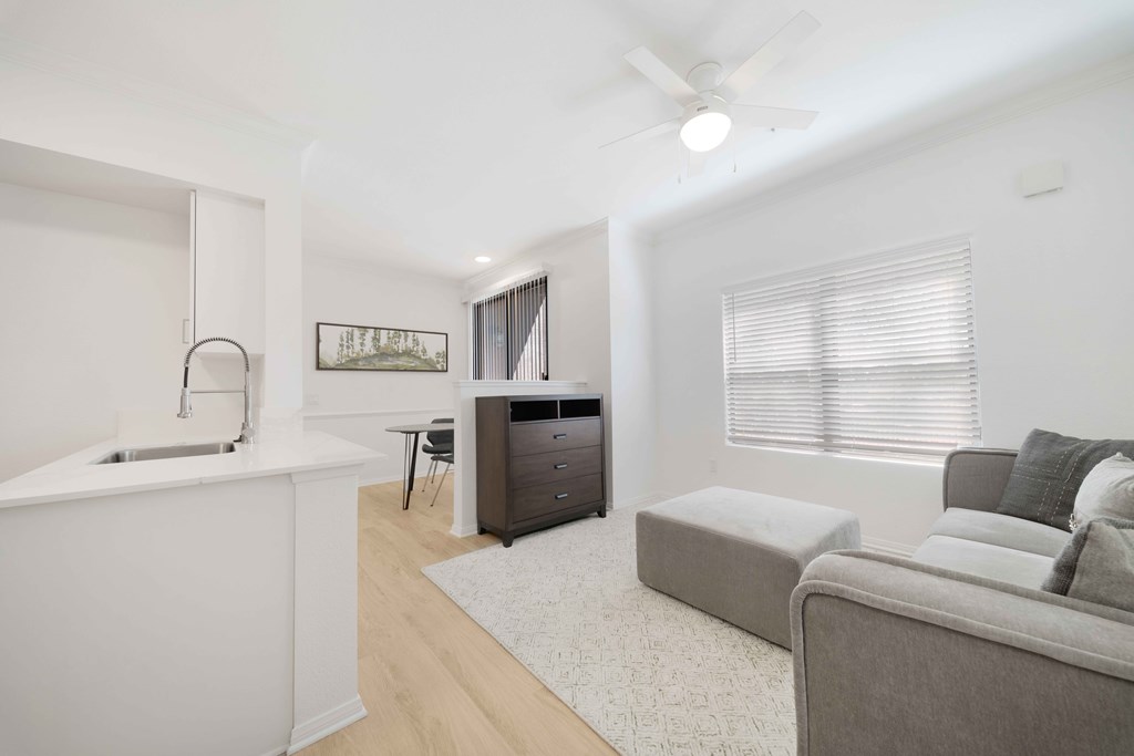 A modern living room with a grey couch and a white kitchen area.