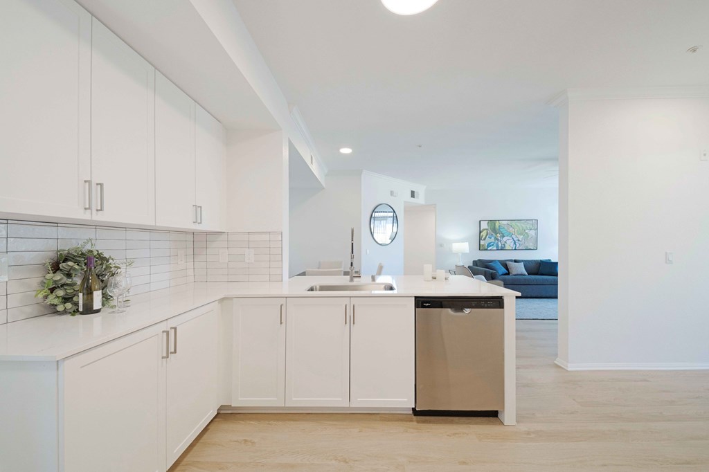A kitchen with white cabinets and a trash can.