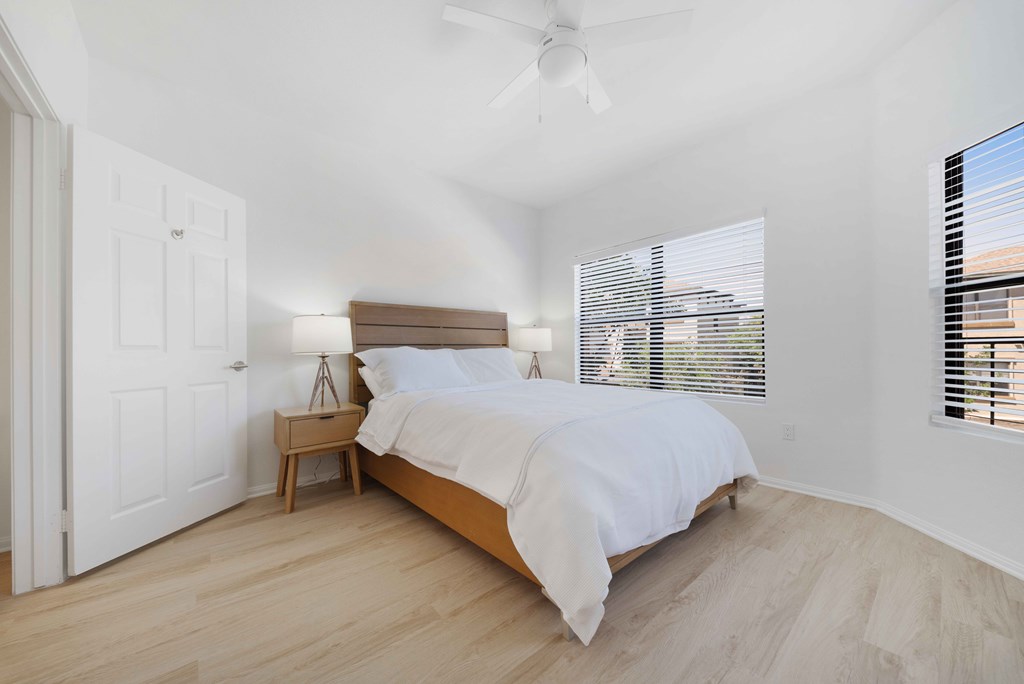 A bedroom with a bed, nightstand, and window with blinds.