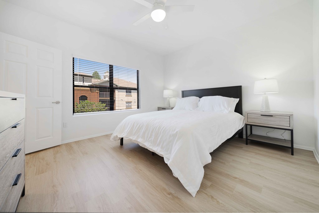 A bedroom with a bed, nightstand, and window with blinds.