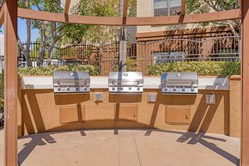 Three barbecue grills are lined up on a patio.