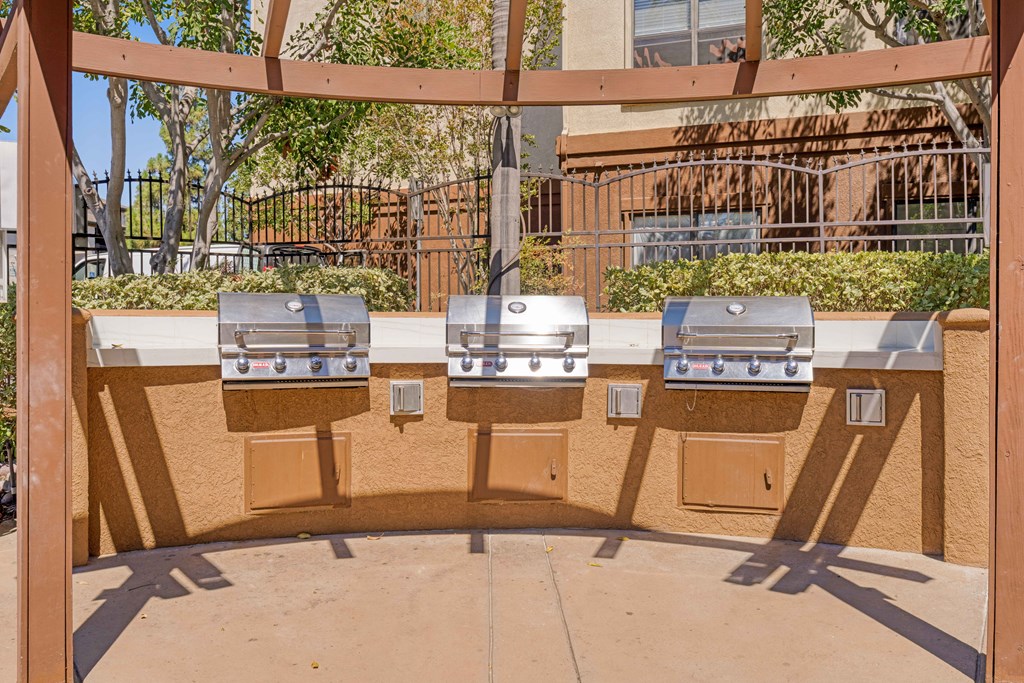 Three barbecue grills are lined up on a patio.
