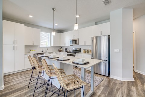 a kitchen with a large island with stools and a stainless steel refrigerator