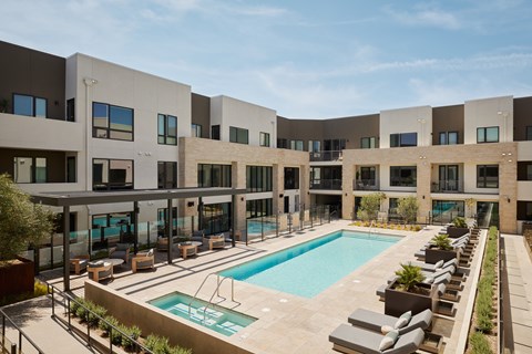 A large swimming pool is surrounded by lounge chairs in front of a building.