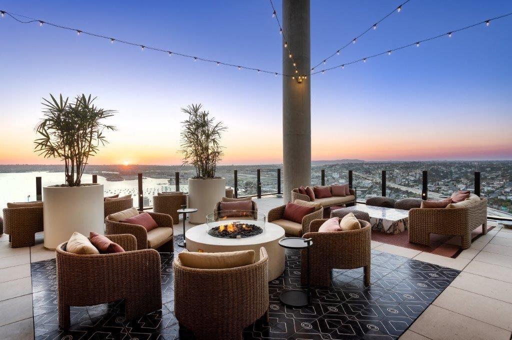 A patio with wicker furniture and a fire pit overlooks a sunset.