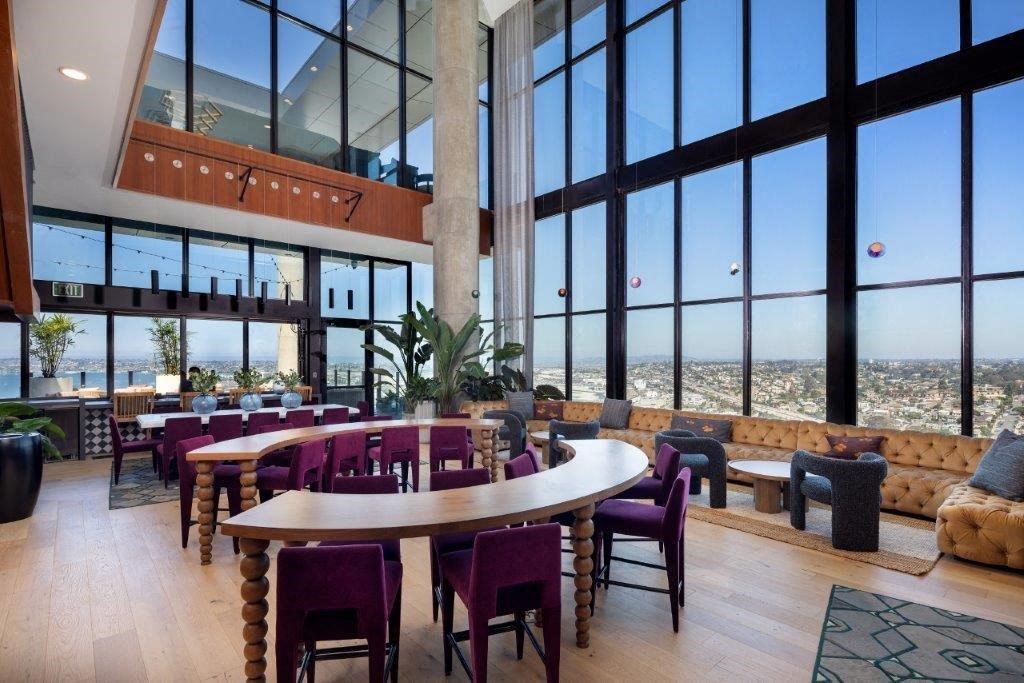 A large round wooden table with chairs around it in a room with large windows.