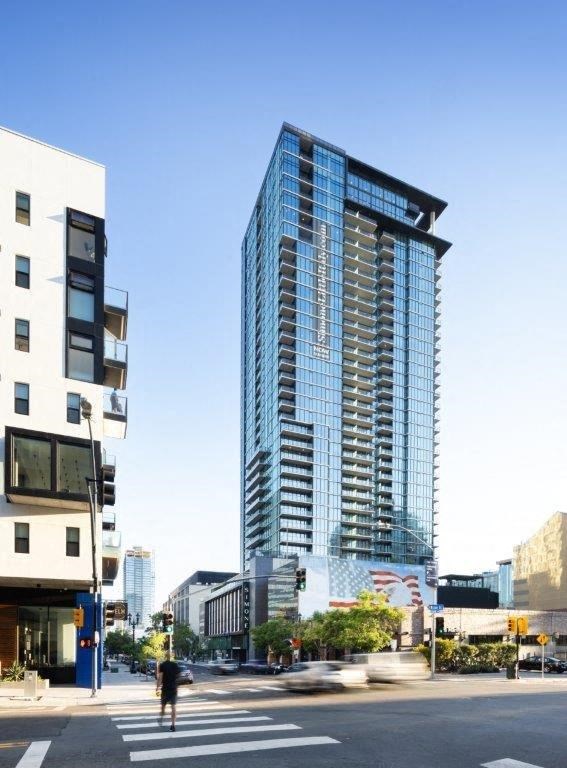 A tall glass building stands next to a smaller white building on a city street.