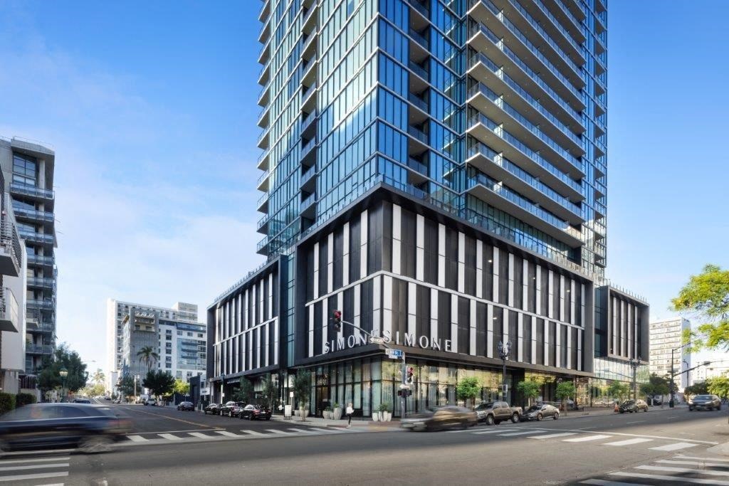 A tall building with a blue glass facade stands in the middle of a city street.