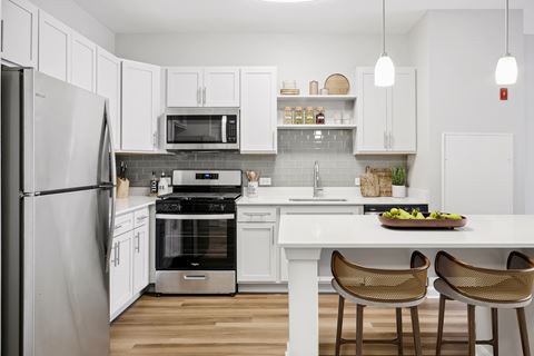 a kitchen with white cabinets and stainless steel appliances and a white island with three chairs