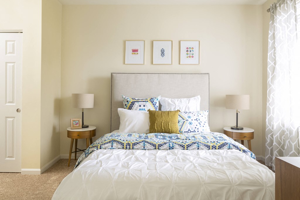 a bedroom with white walls and a bed with a white comforter and blue and yellow pillows
