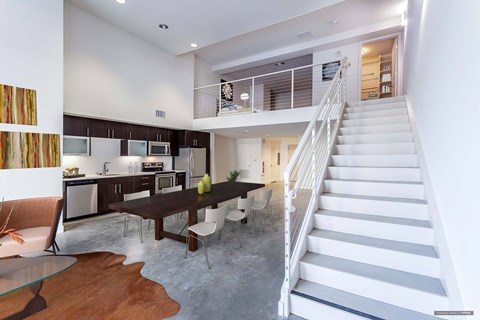A modern kitchen with a dining table and chairs is adjacent to a staircase.