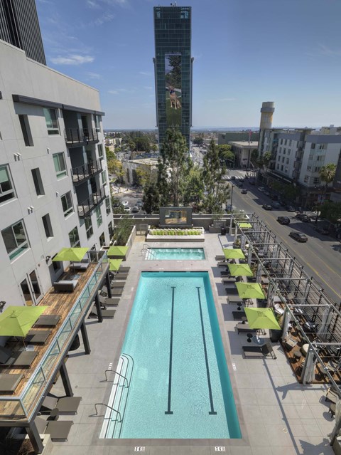 A large swimming pool with lounge chairs and umbrellas on a rooftop.