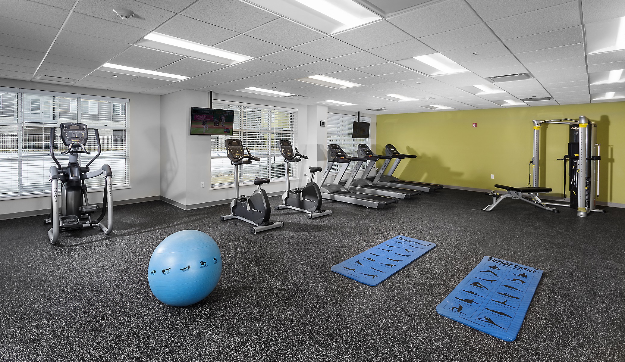 an apartment gym with a yoga ball, yoga mats, tv, stationary bikes, and treadmills