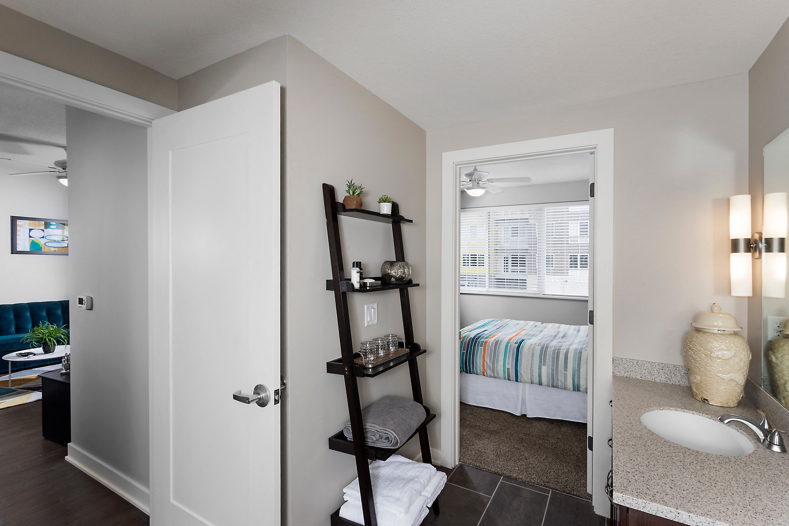 the corner of a bathroom fashioned with a standing bookshelf that is storing bathroom items