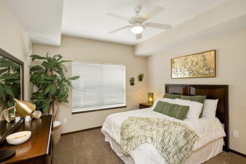 A bedroom with a bed, a ceiling fan, and a painting on the wall.