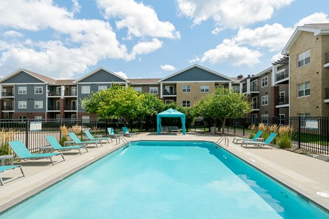 A swimming pool surrounded by sun loungers and apartment buildings.