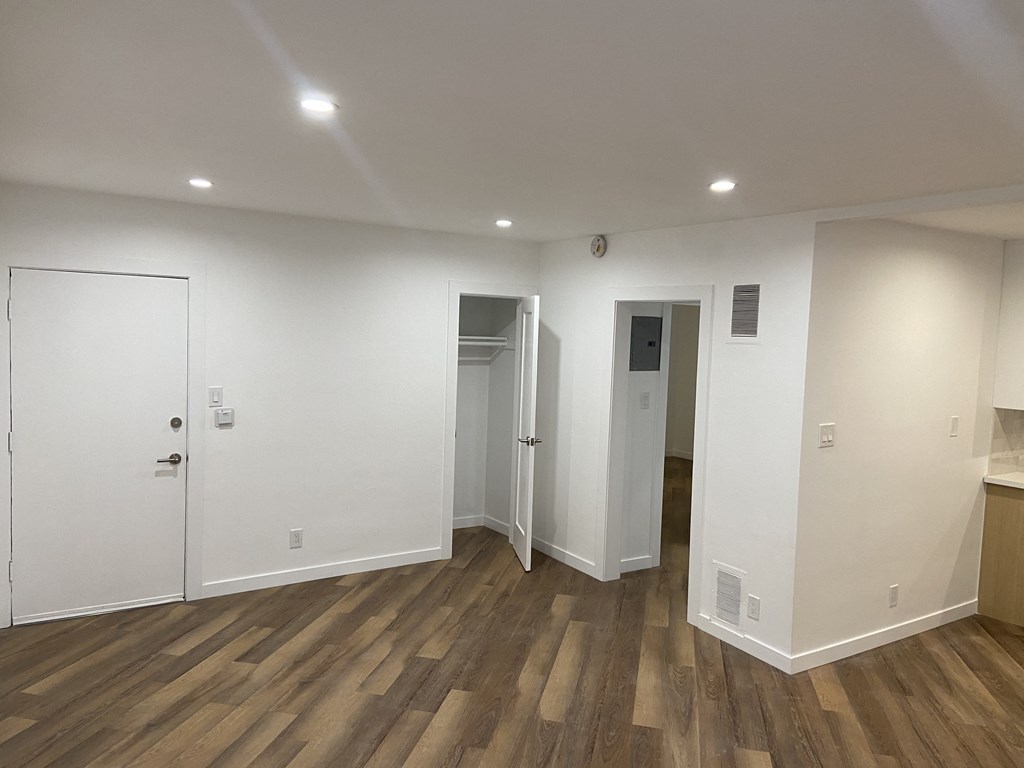a living room with white walls and wooden flooring and a door into a bathroom