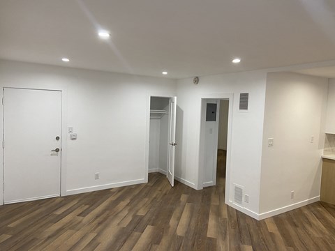 a living room with white walls and wooden flooring and a door into a bathroom