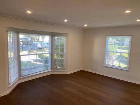an empty living room with two windows and a wooden floor