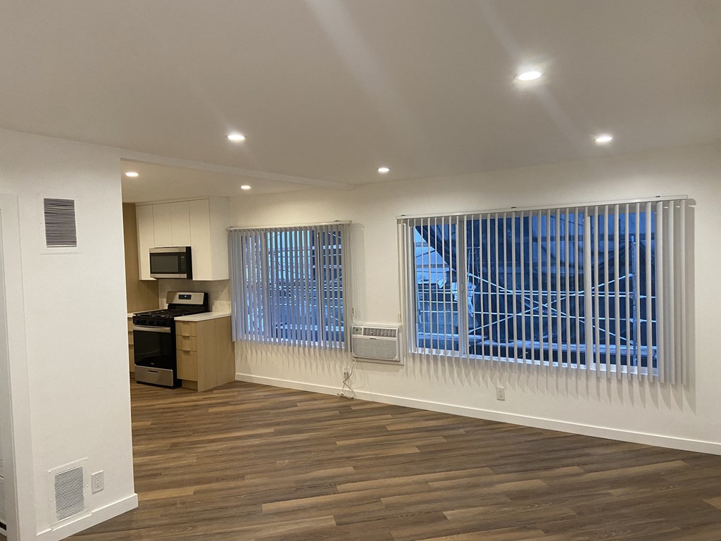 an empty living room with a large window and a kitchen
