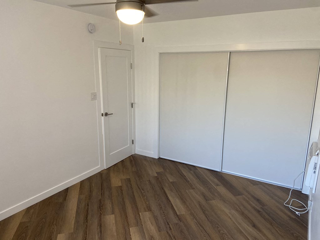 a bedroom with white walls and wood floors and a closet