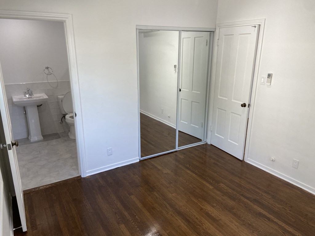 a bedroom with a mirror and a bathroom with a toilet and a sink