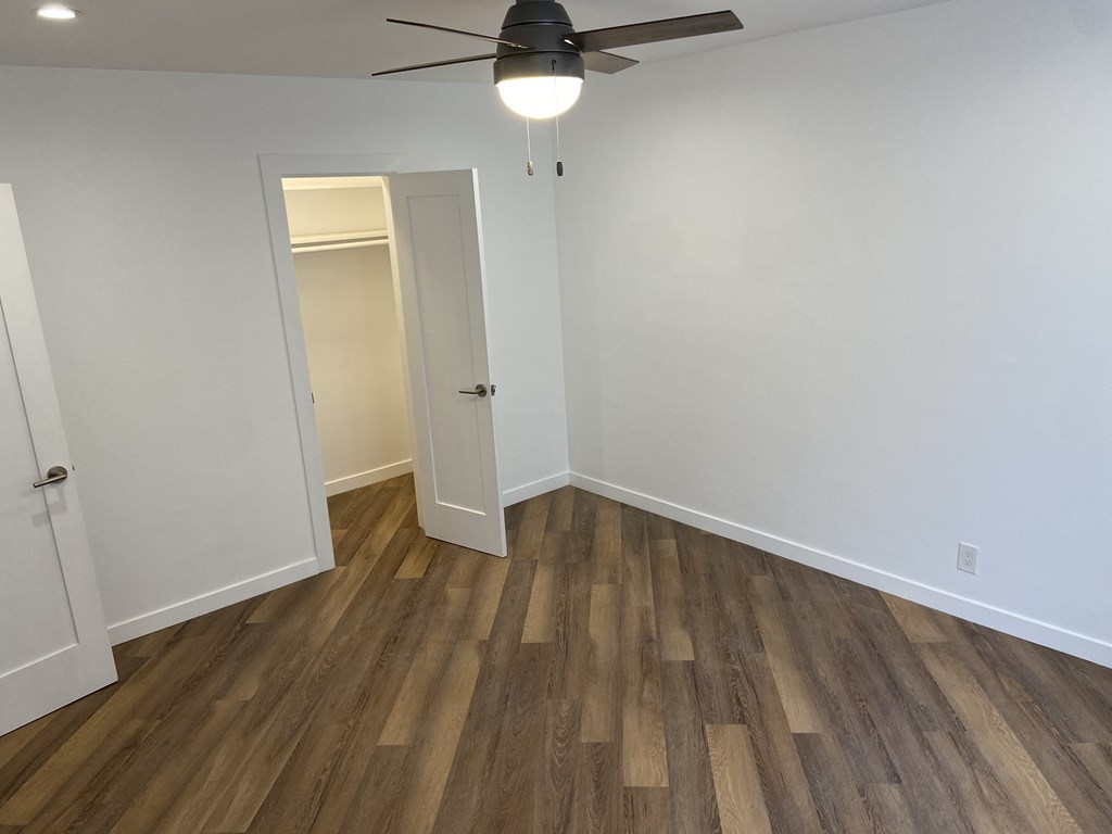 a bedroom with white walls and wood flooring and a ceiling fan
