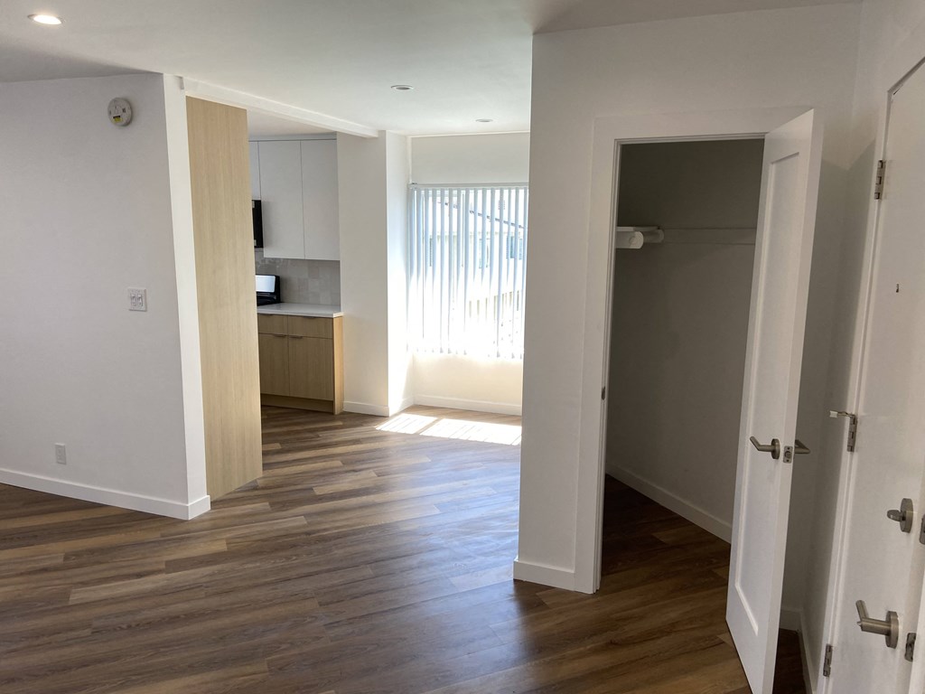 an empty living room with wood flooring and a door to a kitchen