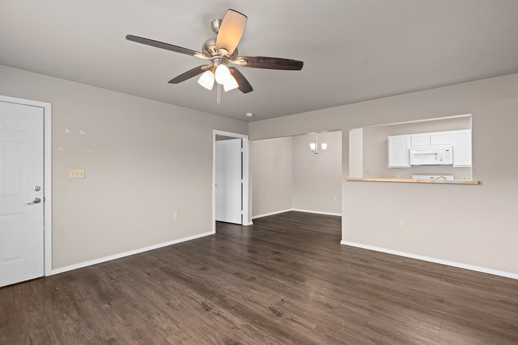an empty living room with a ceiling fan and a kitchen