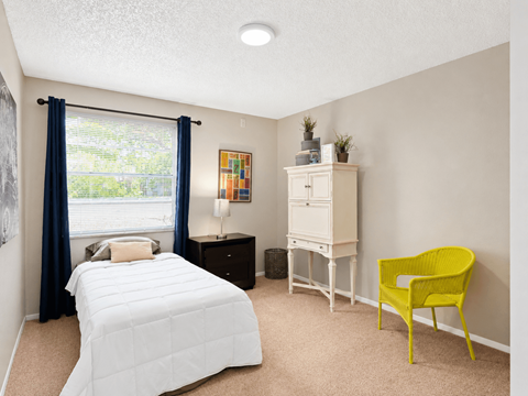 A bedroom with a white bed, a yellow chair, and a white dresser.