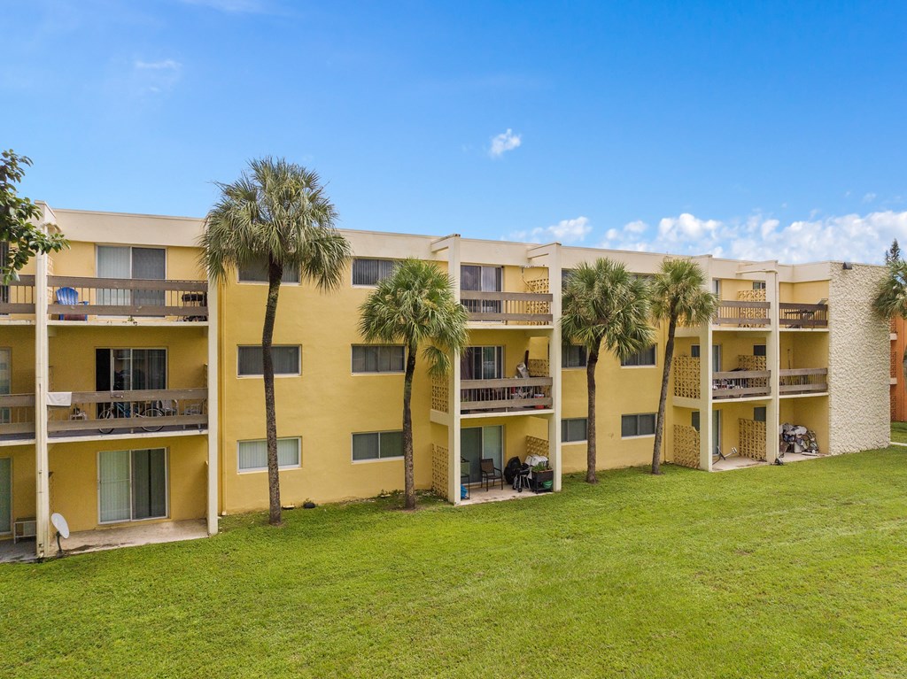 a large yellow apartment building with palm trees in front of it