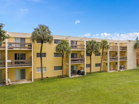 a large yellow apartment building with palm trees in front of it at Cypress Grove, Lauderhill, 33313