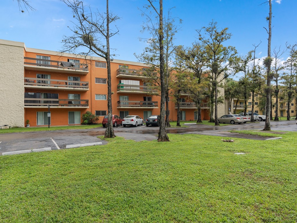 the view of an apartment building with cars parked in a parking lot